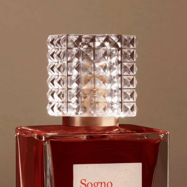Ein eleganter Parfumflakon mit einem kunstvoll gestalteten, klaren Deckel und einem tiefroten Inhalt.