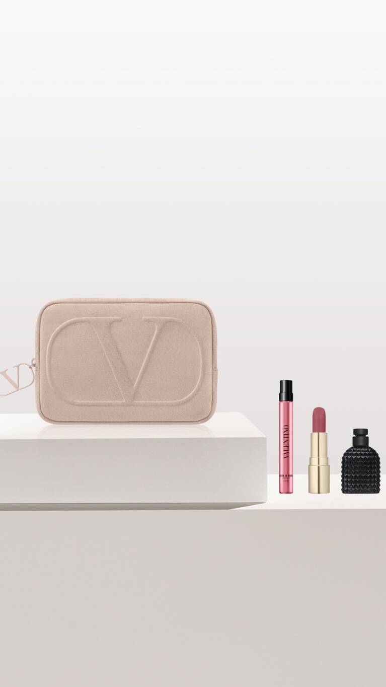 A soft pink cosmetic bag with the initials 'VD' beside three perfume bottles on a clean, minimalist display.